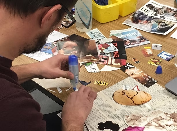 A participant using a glue stick to create a collage with magazine images and words at a shared artmaking table