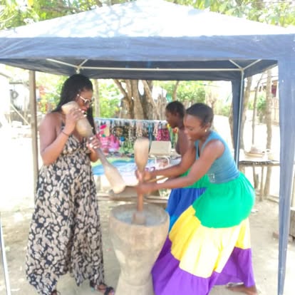 Tye and two women sharing an outdoor activity with a large wooden mortar and pestles