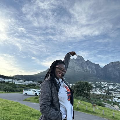Tye smiling in front of a dramatic mountain landscape beneath a cloud-filled sky